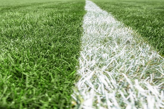 Close up of a baseball on the grass pitch with players in the background