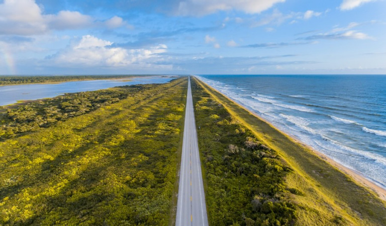 View of a straight road with land and sea either side