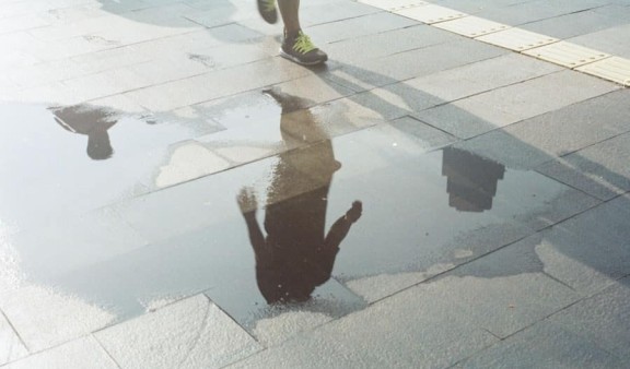 Reflection in a puddle of water of someone walking on a pavement