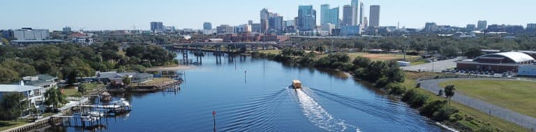 Boat heading down a river with tall office buildings in the distance